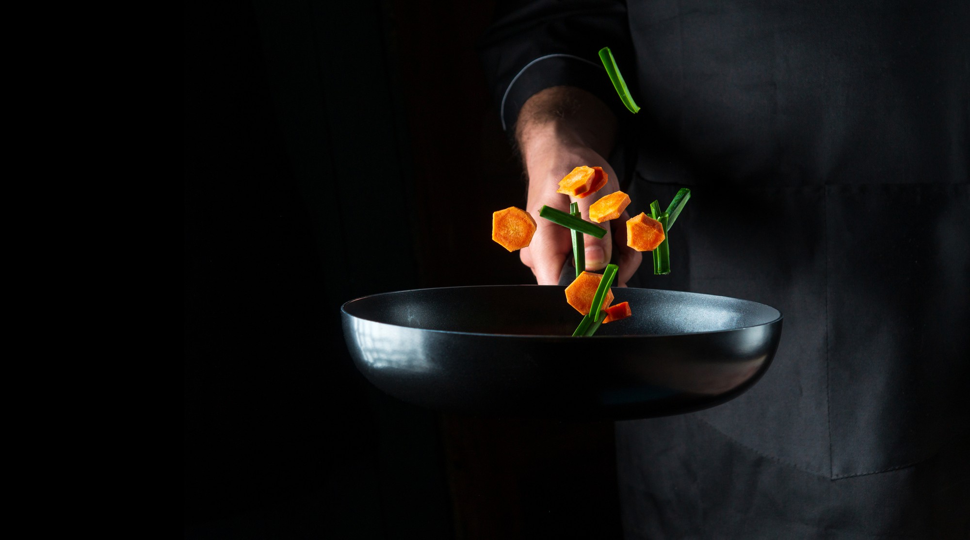 Chef plating a refined dish on dark tableware